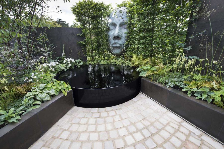 2 low walls, retaining planted beds and faced with Steel Dark DesignClad, meet at round pond at matching oblique angles. 