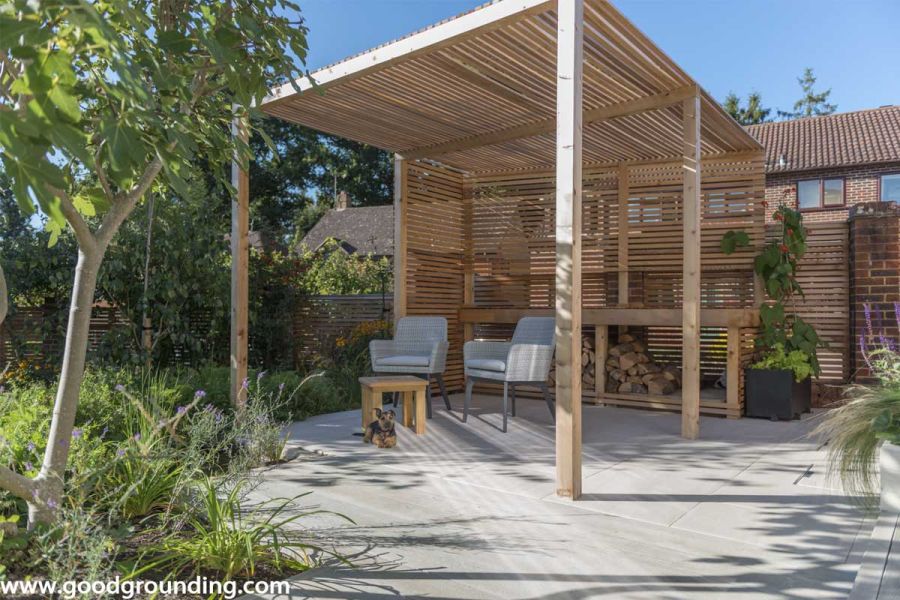 Faro porcelain paving laid under wooden pergola that covers two garden chairs and a coffee table, ideal for relaxing outdoors.