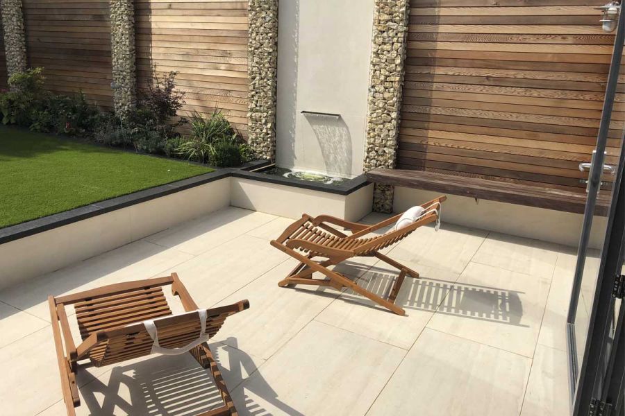 Faro porcelain patio with wooden deck chairs, DesignClad exterior wall cladding water feature on the left, and cedar battens.