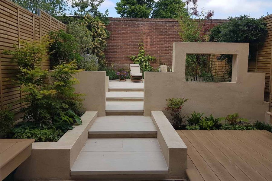 Faro porcelain paving used as wide steps leading up to patio with sunloungers. Decking area to the right.
