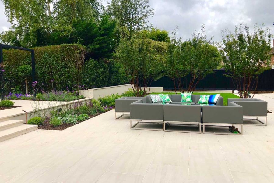 Grey luxury furniture garden set with bright green cushions positioned on a faro porcelain patio, with trees in the background.