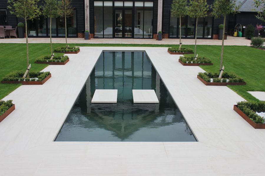 Water feature with porcelain stepping-stones and Faro Porcelain laid around it leading to contemporary house with bi-fold doors.