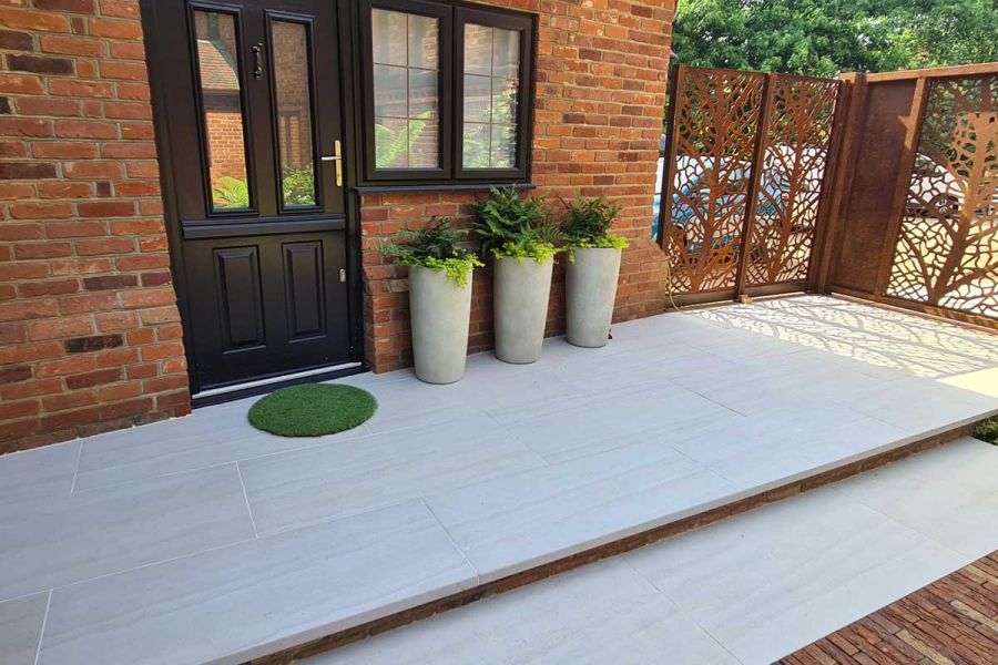 Close view of Faro Porcelain Paving, the patio tiles also used as downstand steps. 3 planters sit on doorstep next to steel corten frames.