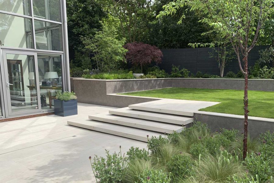 Multi-level garden with Faro porcelain steps and paving from London Stone, Luxury DesignClad and rich planting that includes trees.