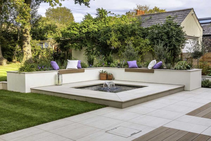Raised square pond with water feature set in Faro Porcelain patio tiles, with raised beds with matching coping on 2 sides.