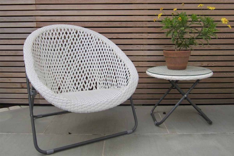 White open weave rattan chair with folding table sits on flamed Grey Smooth Sandstone slabs edged with setts, by cedar fence.