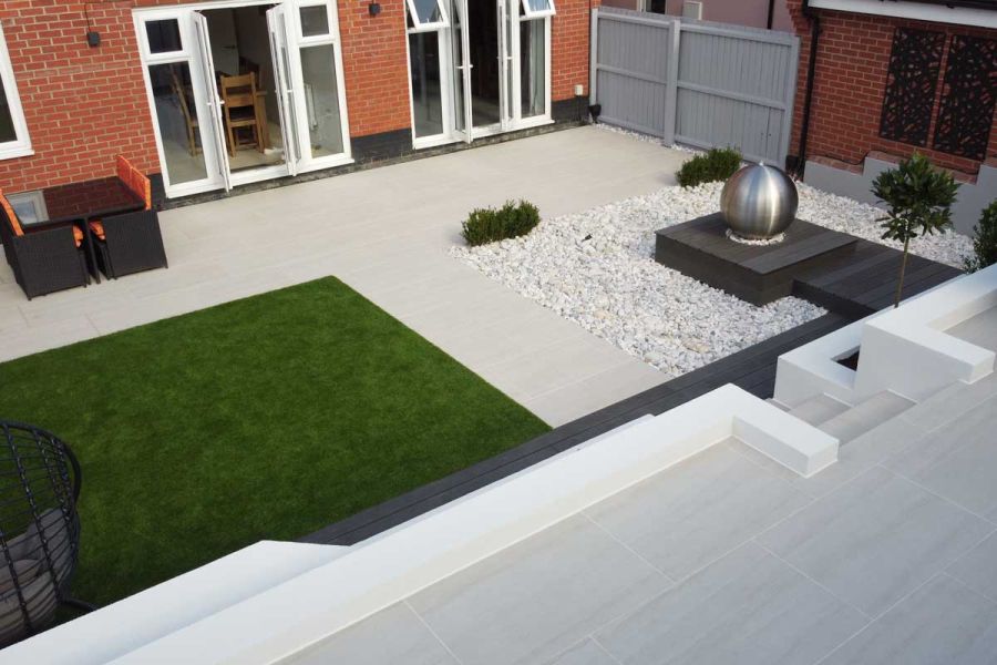View down onto porcelain paving, white pebbles and Charcoal dark grey composite decking, from narrow terrace at rear of garden.