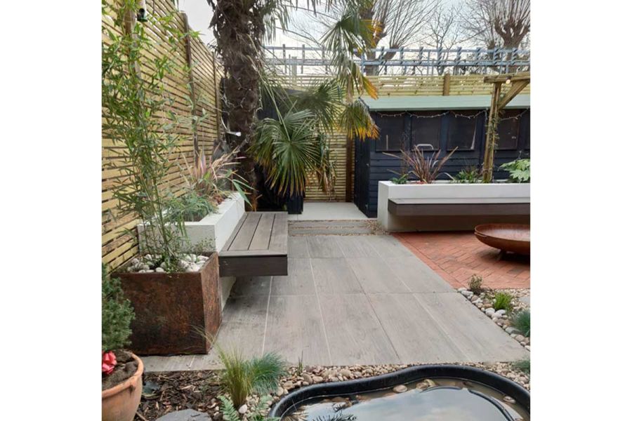 Nuage Porcelain Paving Planks laid parallel to slatted fencing, narrow white raised bed with small plants and attached bench.