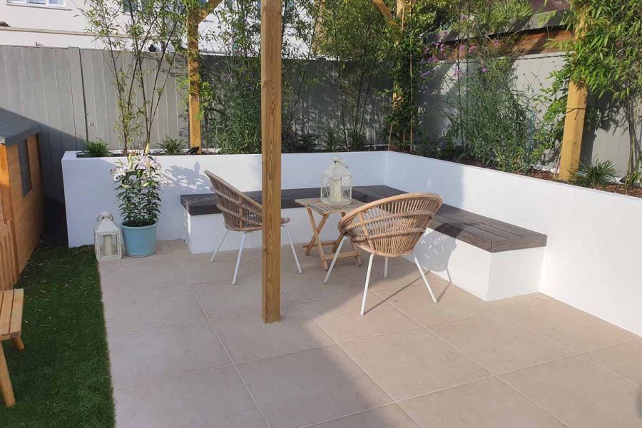 Patio of Florence beige porcelain outdoor tiles, fence behind, with white-rendered raised bed and wooden-topped bench on 2 sides.