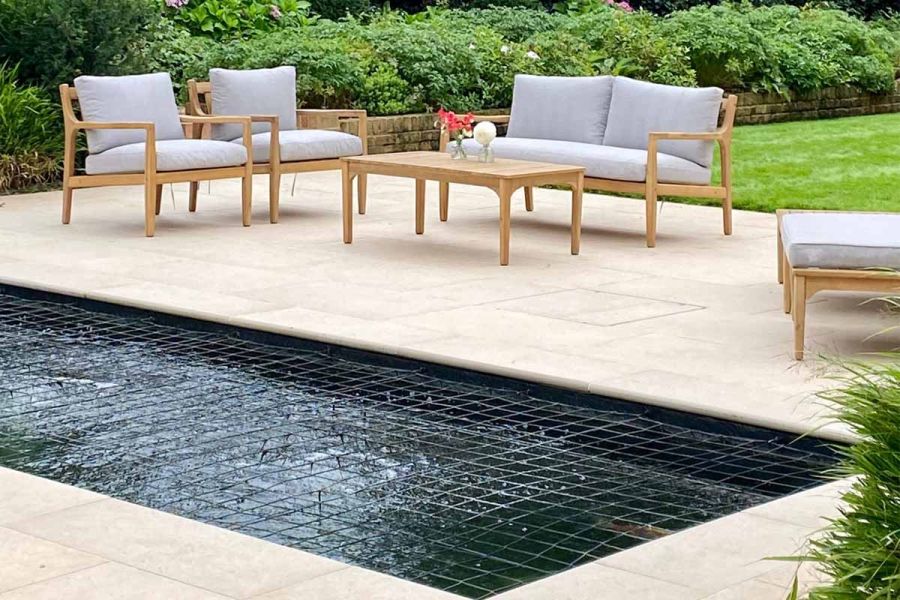 Wood-framed outdoor furniture on Florence Beige patio with matching porcelain coping edging rectangular pond. 