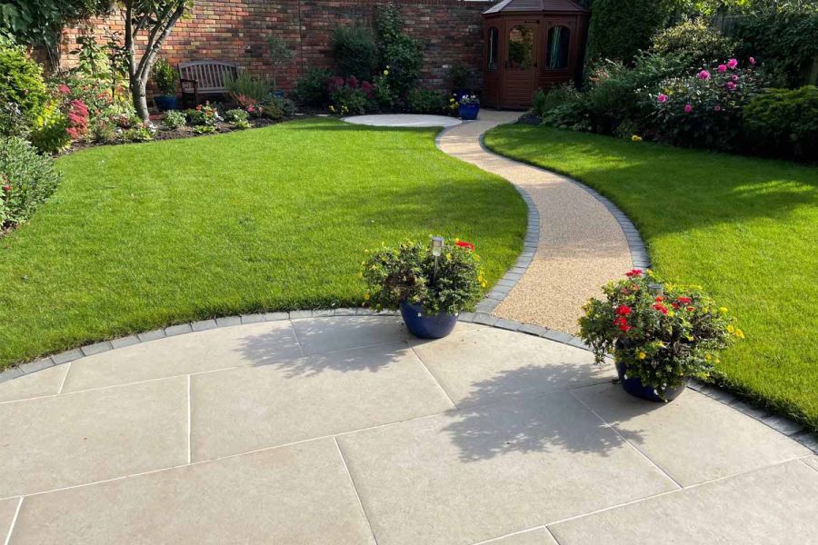 Sinuous resin-bound path edged in dark setts connects curved Florence beige porcelain patio with summer house across the lawn.