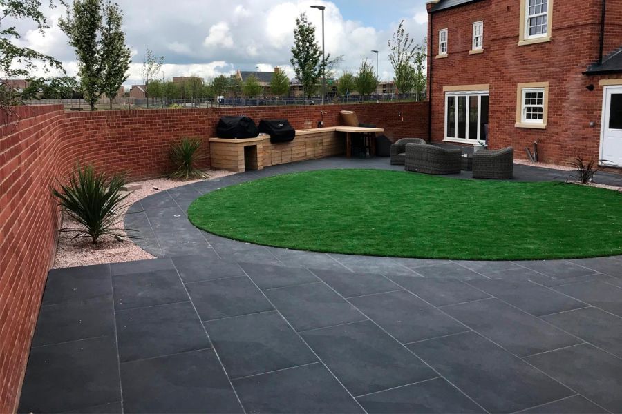 Walled back garden with oval lawn circled by path of Florence Dark outdoor tiles UK. Designed by Muddy Boots Landscaping.