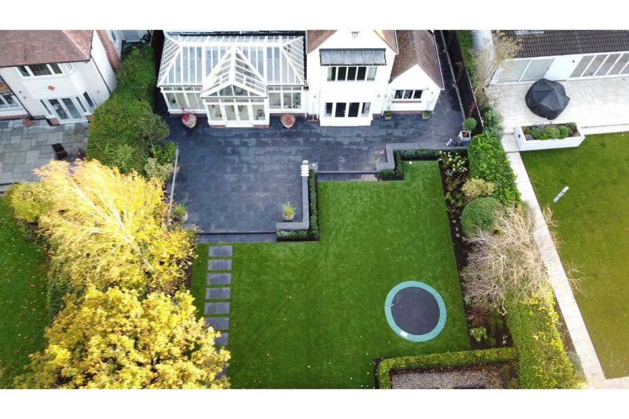 Drone birdseye view of a residential garden looking down on a large dark porcelain patio, artificial lawn and sunken trampoline.