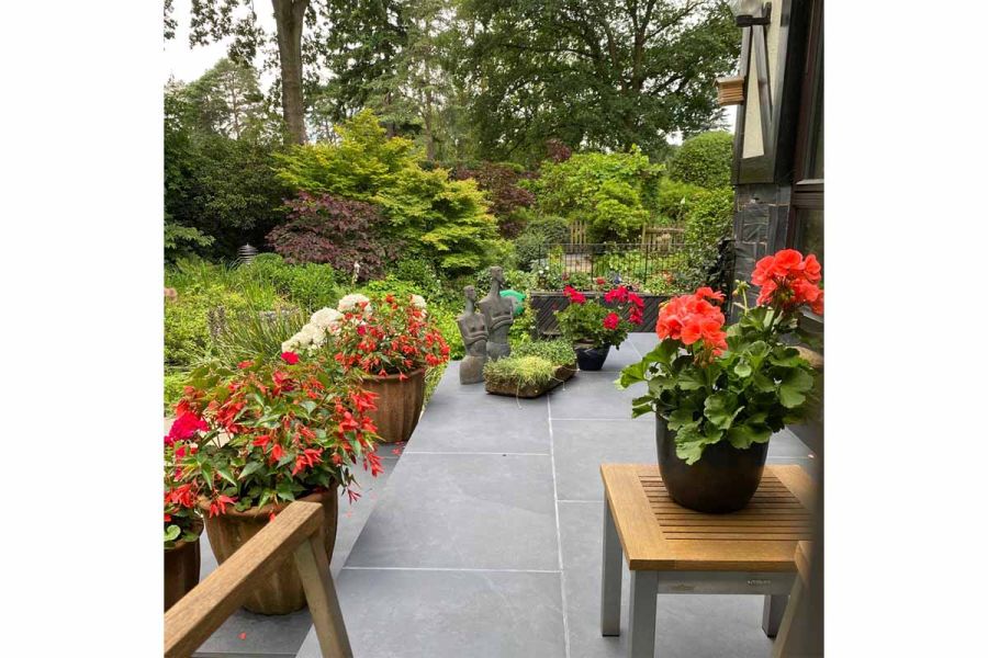 Sculptures and potted geraniums on Florence Dark outdoor tiles UK, lush planting in background, designed by Zutshi Landscaping.