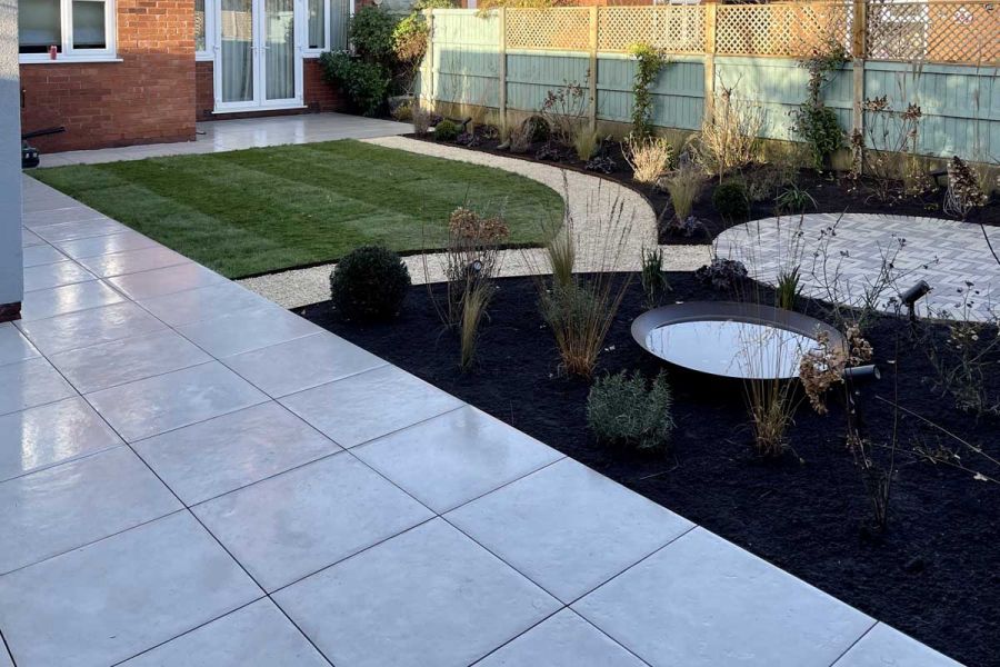 Newly landscaped back garden with a Florence Grey Porcelain patio and a gravel pathway linking together lawns and circular paved area.