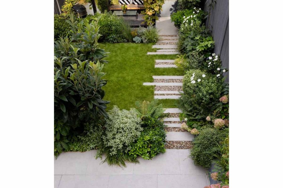 Staggered path of florence grey porcelain paving mixed with pebbles lead up to patio area while densely planted areas line the garden.