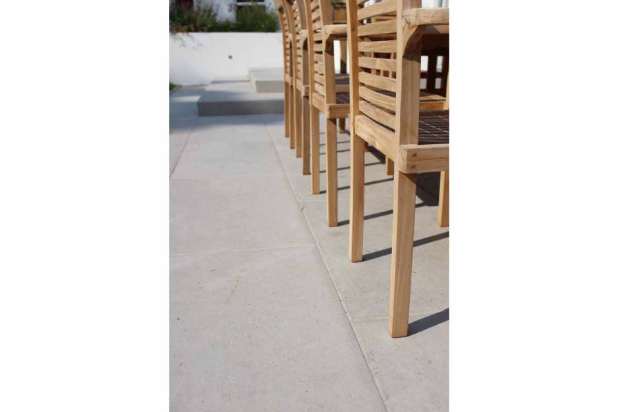 The backs of 4 wooden chairs, seen from one end, on Florence Grey porcelain patio tiles, with matching steps in background.