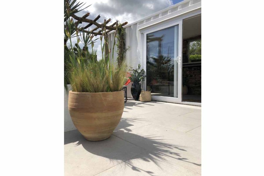 Large round terracotta planter filled with grasses sits on Florence Grey porcelain paving in patio designed for RHS Malvern 2019.