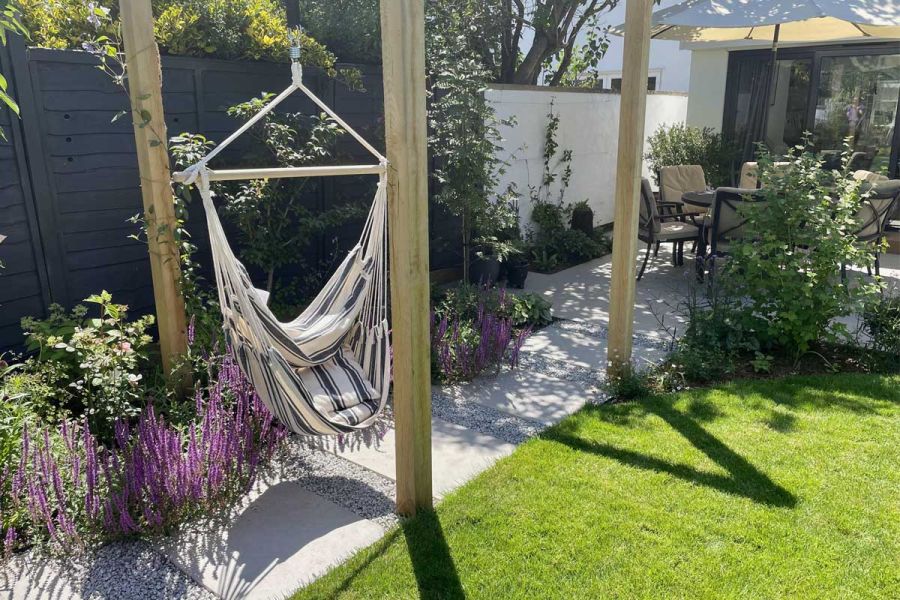 Hammock hangs over path of Florence Grey porcelain leading from patio between lawn and planted border. Design by Emily Jane Bones.