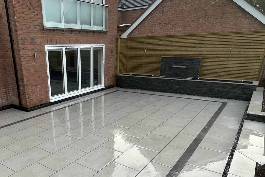 Wet rectangular Florence Grey patio with black outline outside french doors, with 2 steps up to lawn  of sloping fenced garden.