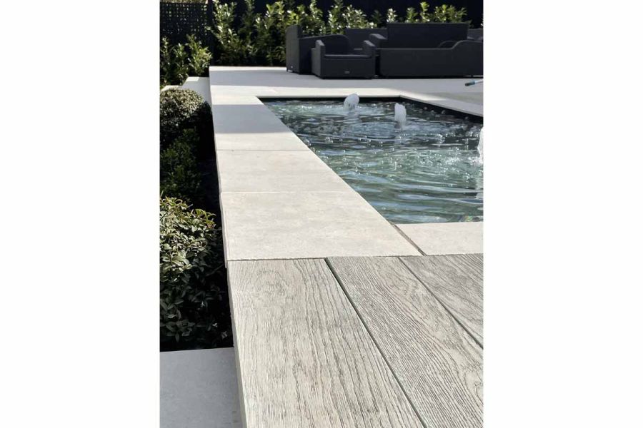 Florence grey porcelain paving surrounds rectangular pond with 3 bubbling water spouts. Smoked oak Millboard decking in foreground.