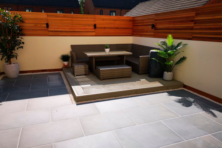 Rattan lounge set on decking dais in corner of garden, surrounded by Florence Storm porcelain paving. Design by SB Outdoor Living.