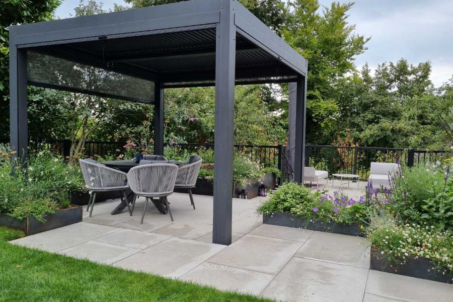 Raised beds beside metal pergola over dining set on Florence White porcelain slabs. Design by Adam Vetere. Built by JJH Landscapes.