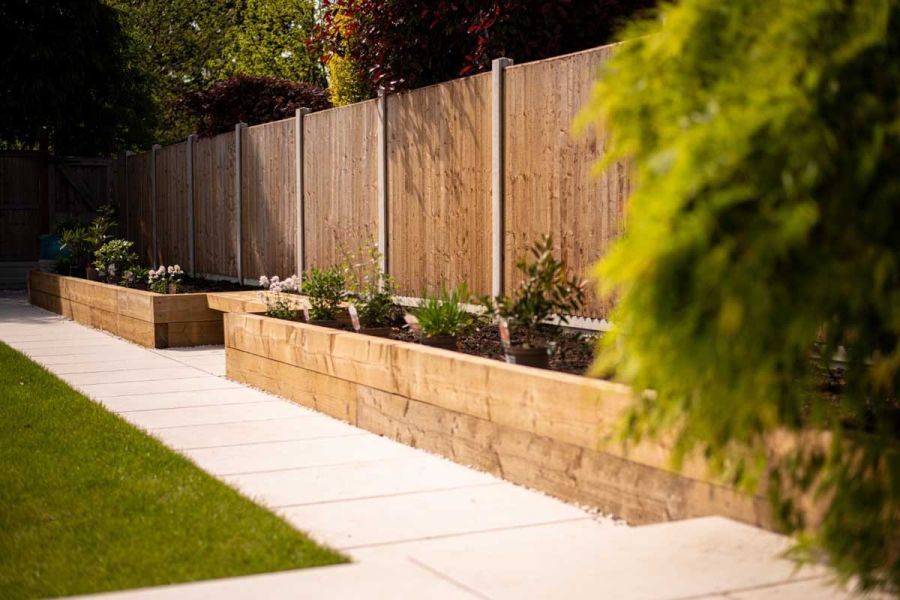 Florence White Porcelain path leading down a back garden with a lawn on one side and raised timber sleeper flower beds on the other.