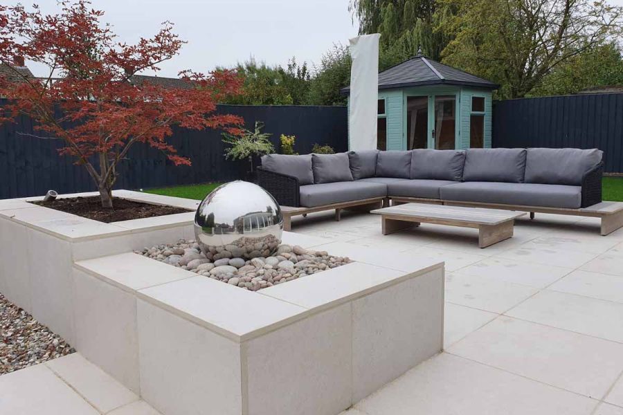 Florence white porcelain outdoor tiles UK paves patio and faces raised trippett and water feature with pebbles and silver ball.