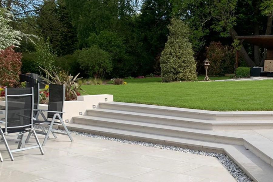 Garden furniture sits on Florence White porcelain paving, with strip of grey garden pebbles at base of 4 steps in matching slabs.