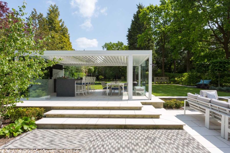 Raised patio area using Florence White Porcelain paving with steps used in the same, under a white pergola surrounded by large trees