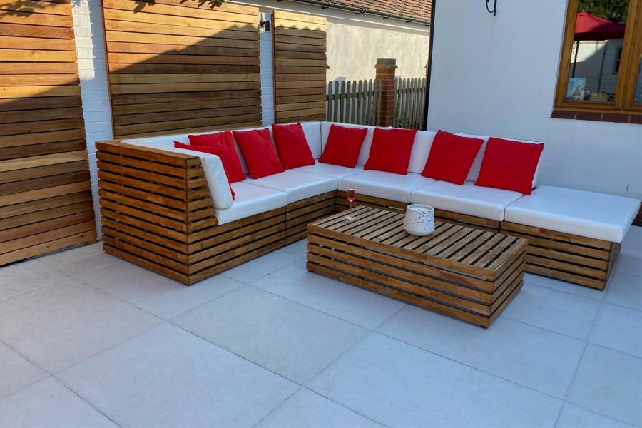 Corner sofa set, made of wooden battens, with white and orange cushions, sits on Florence white porcelain paving, laid stack bond.