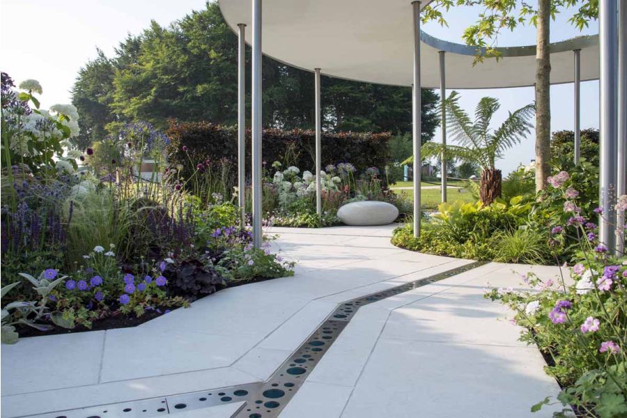 Bespoke-cut Florence White porcelain slabs pave show garden. Modern metal grille covers rill leading to central round flower bed.