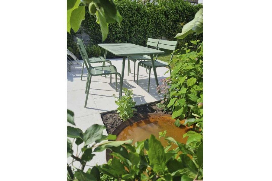 Green-painted garden furniture sits on Florence White porcelain paving between hedge and flowerbed. Design by Northern Landscapes.