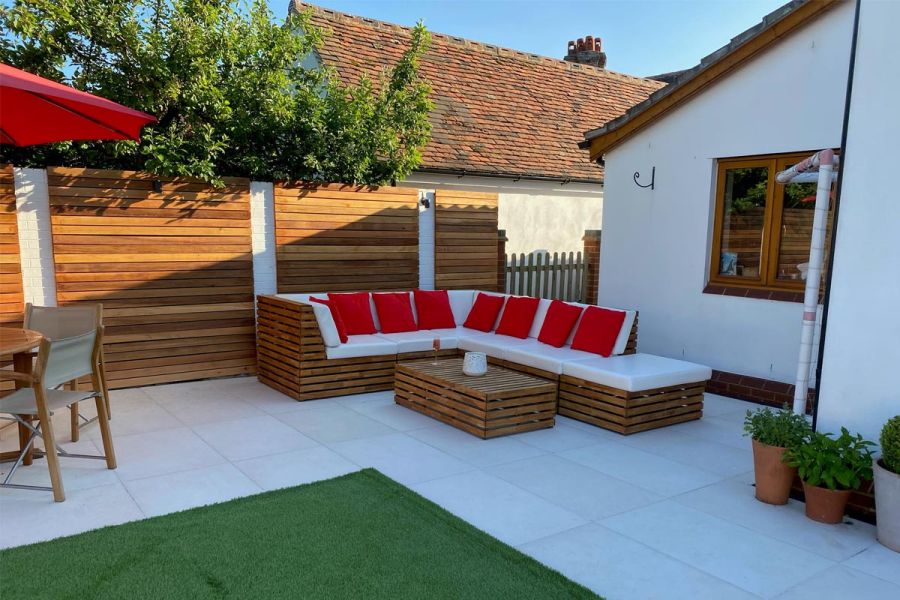 L-shaped patio in Florence White Porcelain paving slabs, with corner sofa and coffee table of slatted wood to match the fence.