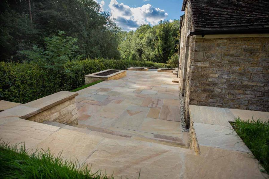 Steps descend from grass to rectangular paved area of Camel Dust Indian sandstone slabs to side of rural cottage. 
