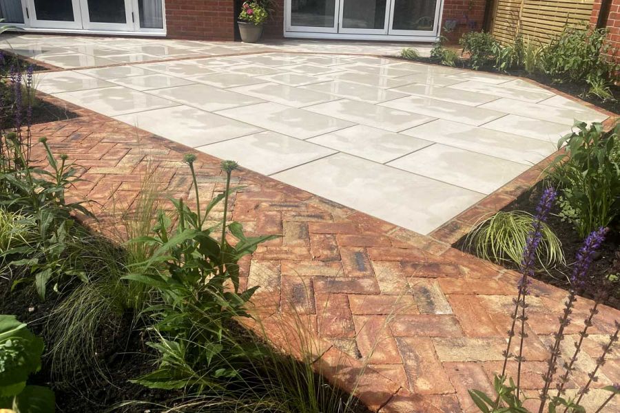 Cream paving slabs edged by Cotswold clay pavers and brick path outside 2 sets of french doors. Built by Essex Garden Designs.