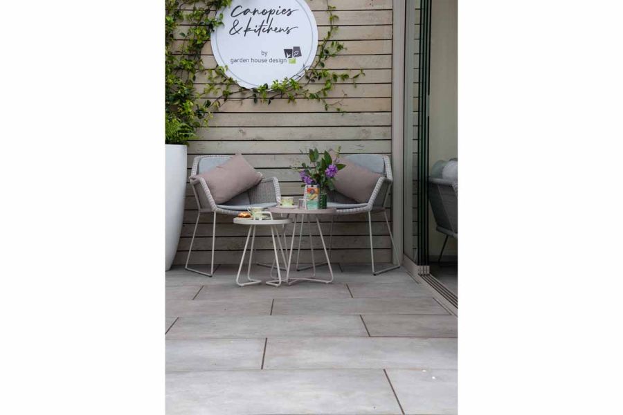2 metal chairs and tables next to tall planter on Garden House Design trade stand paved with Venetian Grey Porcelain slabs.