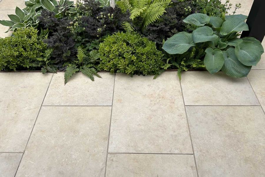 Lush low planted flower bed spilling over the edge of a Jura Beige Porcelain patio that’s jointed with dark grey grout.