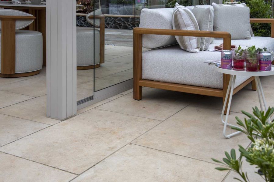 Outdoor tiles UK with natural stone look holds a sofa on Jura Beige Porcelain Paving  with small table holding drinks next to it.