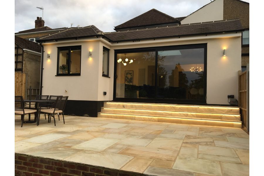 3 steps with undertread lighting descend from modern extension with wide sliding doors to Mint Indian sandstone patio.