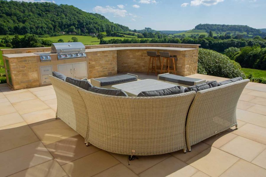 Rattan furniture on buff smooth sandstone paving slabs in mixed sizes, with view over fields to distant horizon. 
