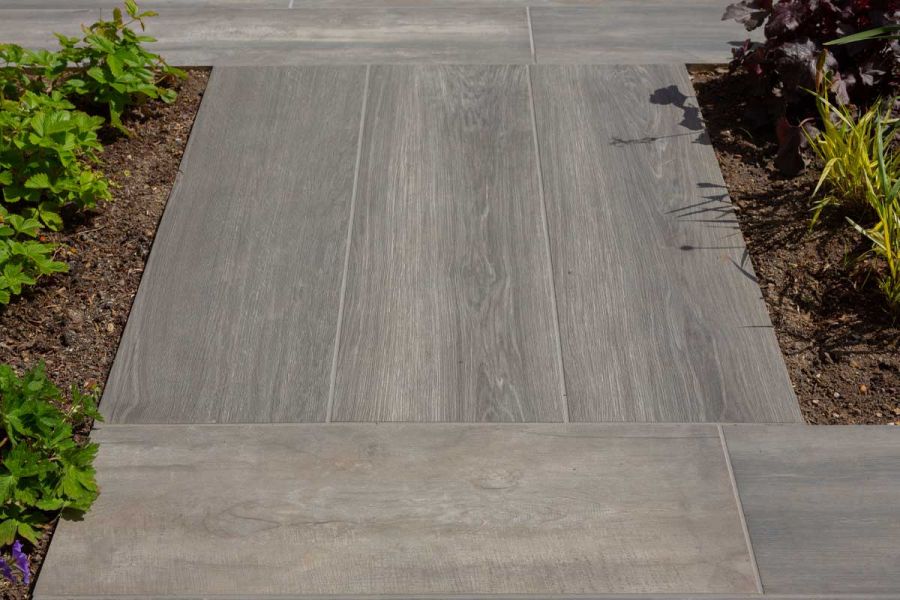 Cinder wood effect porcelain paving slabs grouted with light grey grout and adjoined to low level flower beds.