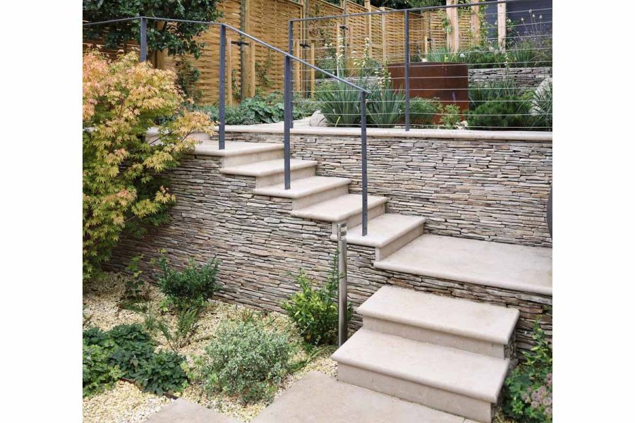 Seamless integration of Jura Beige Smooth Limestone bullnose steps into paving area, with lush green planting.