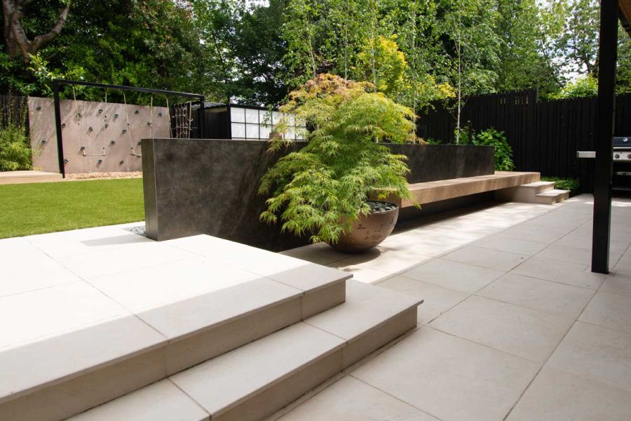 2 large Slab Khaki garden steps rise from matching paving to lawn area. Design by Robert Hughes. Built by Brockstone.
