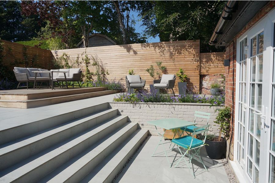 Wide set of Light Grey Porcelain steps leading to a raised decking seating area surrounded by timber screens with climbing plants.