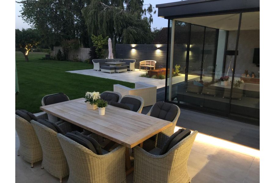 8 seater outdoor dining table adjacent to large glass extension looking down towards another paved seating area and large rural garden.