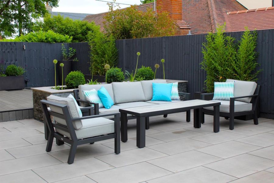 Metal lounging set in a rear back garden paved with Polished Concrete porcelain in front of a raised composite decking area.