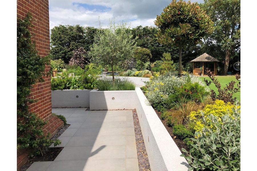 Path down the side of house paved in Steel Grey porcelain with retaining walls leading to an upper terrace of lawn and planting.