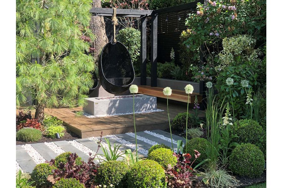 Black Granite plank paving and white pebble path runs past wooden deck with suspended egg chair. Design by Gardens of the Future.